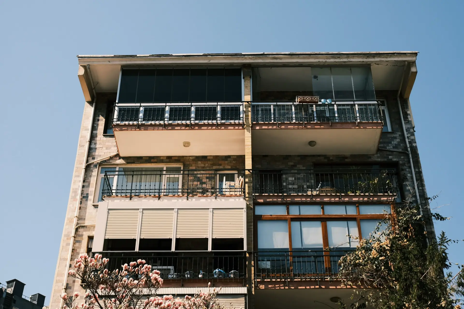 A modern apartment building facade with blooming flowers in the foreground under a clear blue sky.