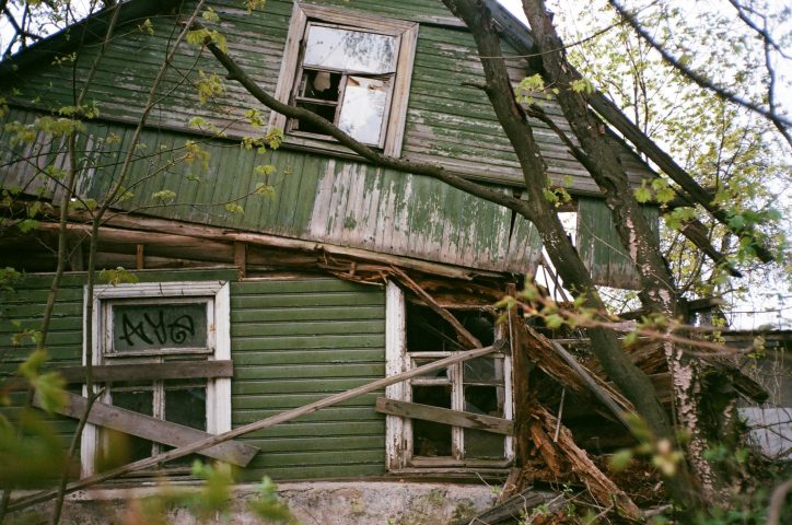 An abandoned rustic house surrounded by trees, showcasing decay and natural overgrowth.